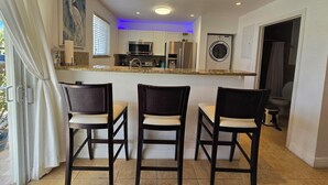 A kitchen with a microwave, refrigerator, and washing machine, a dining area with three chairs, and a view of the outside. - Luxury Ocean Villa 3 Bed / 3 Bath in Bimini Bay (Bimini)