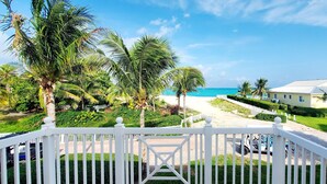 A view from a balcony overlooking a beach with palm trees, a golf cart, and a house with a white fence. - Luxury Ocean Villa 3 Bed / 3 Bath in Bimini Bay (Bimini)