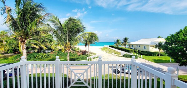 A view from a balcony overlooking a beach with palm trees, a golf cart, and a house with a white fence.
