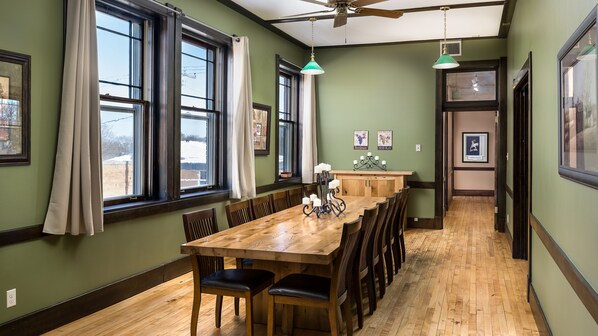 A dining area with a wooden table and chairs, large windows with curtains, and a ceiling fan.