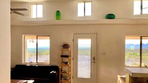 A room with a black sofa, a wicker chair, a bookshelf, and a door leading to a balcony with a view. - Big Bend Getaway: Classic Adobe with Modern Flair (Terlingua)