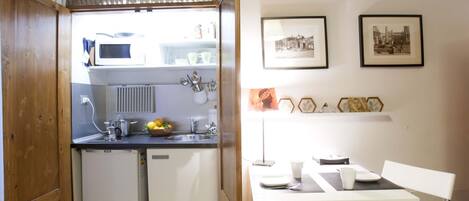 Eine kompakte Küche mit Mikrowelle, Spüle und kleinem Kühlschrank. Es gibt einen Essbereich mit Tisch und Stühlen, sowie zwei gerahmte Bilder an der Wand.