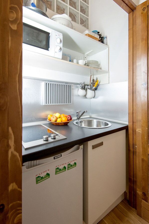 A compact kitchen with a microwave, sink, and a bowl of fruit on the counter.