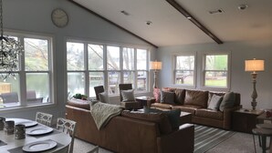 A spacious living room with a large window, a dining area with a table set for four, and a cozy seating area with two couches and a coffee table.