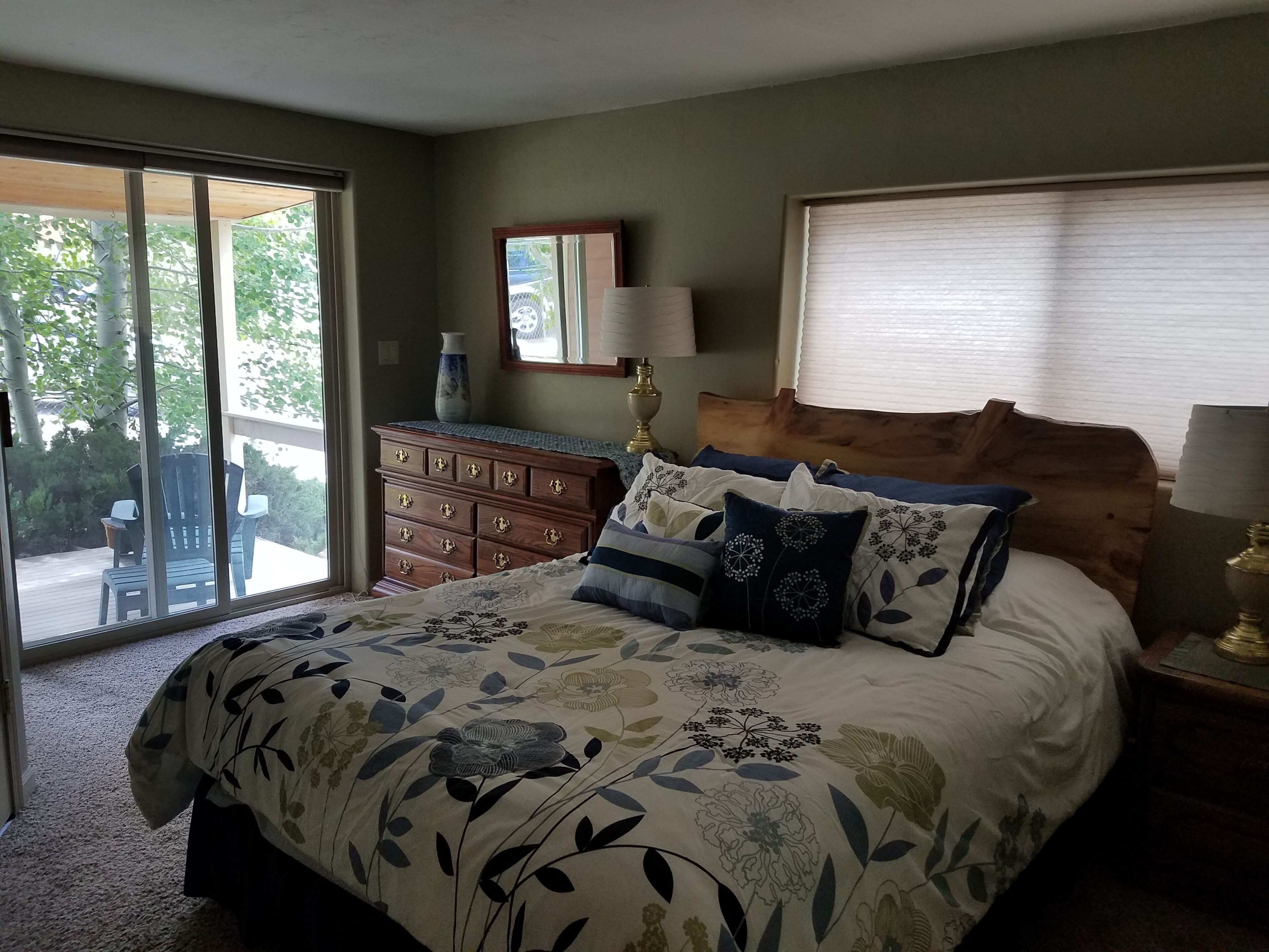 A bedroom with a large bed, a dresser, a nightstand, a mirror, and a window with blinds.