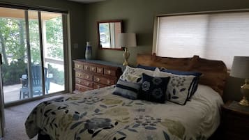 A bedroom with a large bed, a dresser, a nightstand, a mirror, and a window with blinds.