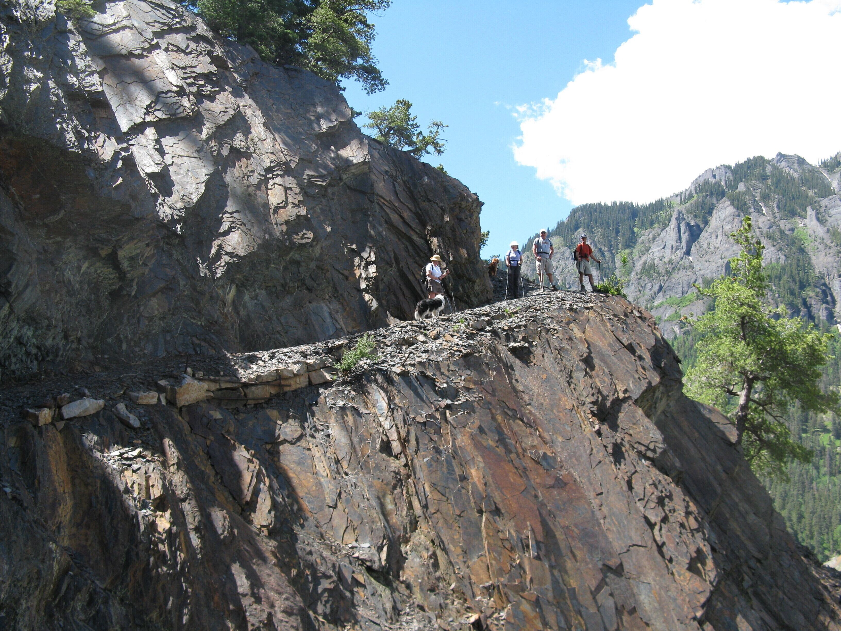 A group of hikers on a rocky mountain ridge with a forested valley in the background.