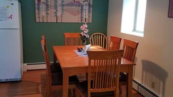 A dining area with a wooden table and chairs, a vase with flowers, a painting on the wall, and a window providing natural light.