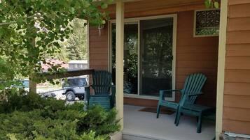A wooden house with a porch, two green chairs, and a stone pathway leading to the entrance.