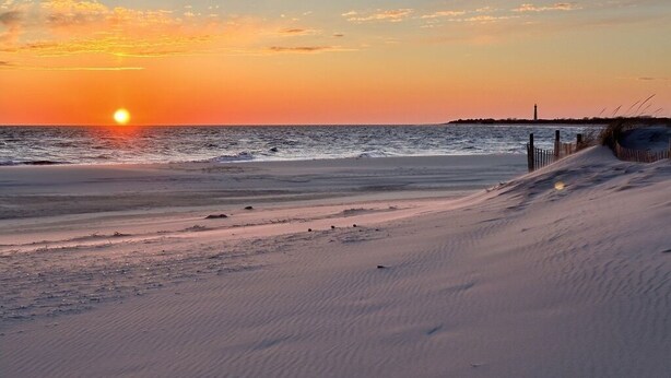 A beach at sunset with a lighthouse in the distance.