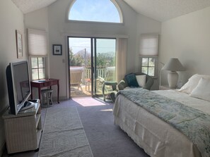Quarto com cama, escrivaninha, cadeira, televisão e varanda.