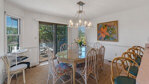 A dining area with a glass table surrounded by wicker chairs, a chandelier, and a painting on the wall.