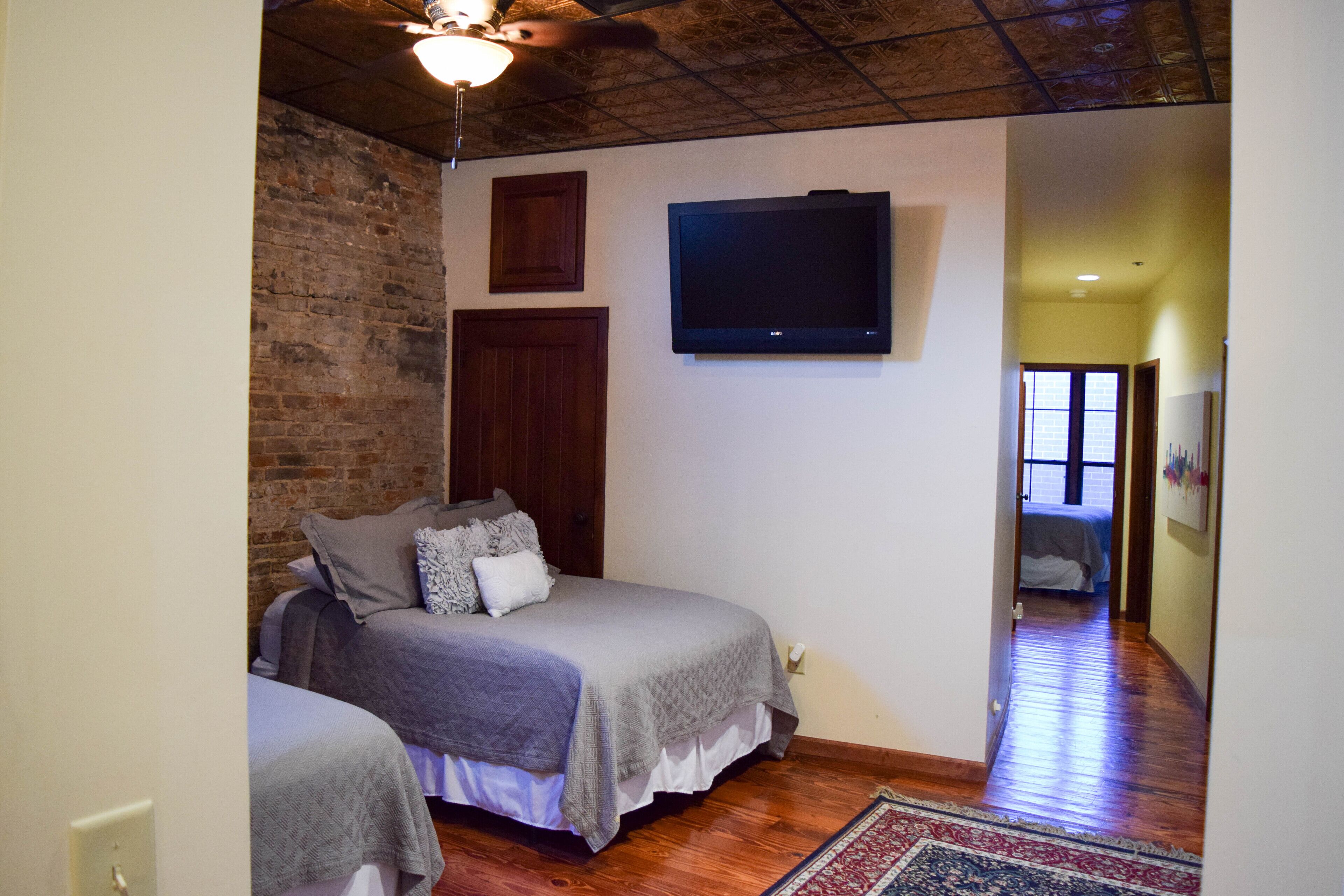 A bedroom with a brick wall, a flat-screen TV, and a wooden ceiling fan.