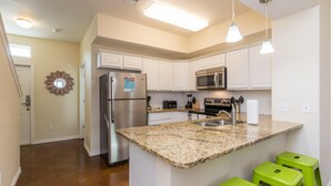 A modern kitchen with white cabinets, a granite countertop, stainless steel appliances, and green bar stools. - Family-Friendly Townhome | Heated Pool, Patio & Beach Nearby (Corpus Christi)