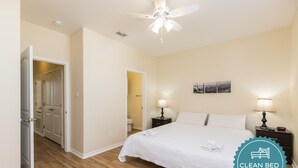 A clean, well-lit bedroom with a large bed, two bedside tables with lamps, a ceiling fan, and a door leading to another room. - Family-Friendly Townhome | Heated Pool, Patio & Beach Nearby (Corpus Christi)