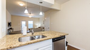 A kitchen with granite countertops, a stainless steel sink, and a dishwasher. There is a ceiling fan and pendant lighting. - Family-Friendly Townhome | Heated Pool, Patio & Beach Nearby (Corpus Christi)