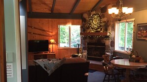 Un salon chaleureux avec une cheminée en pierre, des murs en bois, un téléviseur et un coin repas comprenant une table et des chaises.