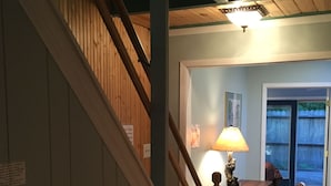 Un escalier en bois mène à un palier où se trouvent une lampe et une petite table. On aperçoit un chien au fond.