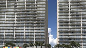 Uma praia com vários edifícios altos ao fundo, cadeiras de praia, guarda-sóis e um céu claro.