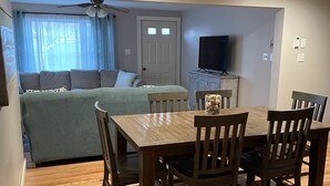 Una sala de estar acogedora con una mesa de comedor de madera, sillas, un sofá y un televisor.