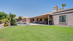 Una propiedad residencial con piscina, patio con sillones de descanso y césped bien cuidado.