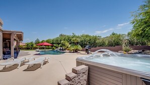 Un jardín con jacuzzi, sillas de descanso, piscina y un paraguas rojo.