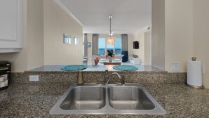 Une cuisine dotée de plans de travail en granit, d’un évier double et offrant une vue sur l’océan grâce à de grandes fenêtres.