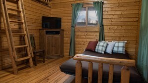 Habitación de cabaña de madera con cama, televisor en un mueble, escalera y ventana con cortinas.