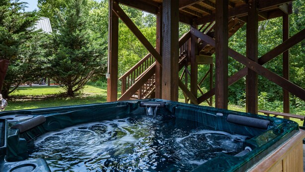 Un jacuzzi en un pabellón de madera con vistas a un césped y árboles.