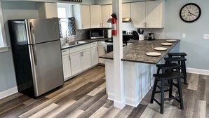 A modern kitchen with white cabinets, a stainless steel refrigerator, a microwave, and a clock on the wall.