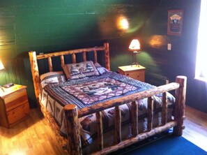 Un lit en bois rustique, agrémenté d’une courtepointe, avec deux tables de chevet et une lampe fixée au mur.