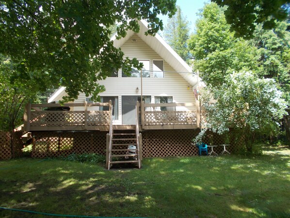 Une maison à deux étages dotée d’une terrasse en bois, d’une échelle menant à l’étage supérieur et d’un petit espace de détente extérieur.