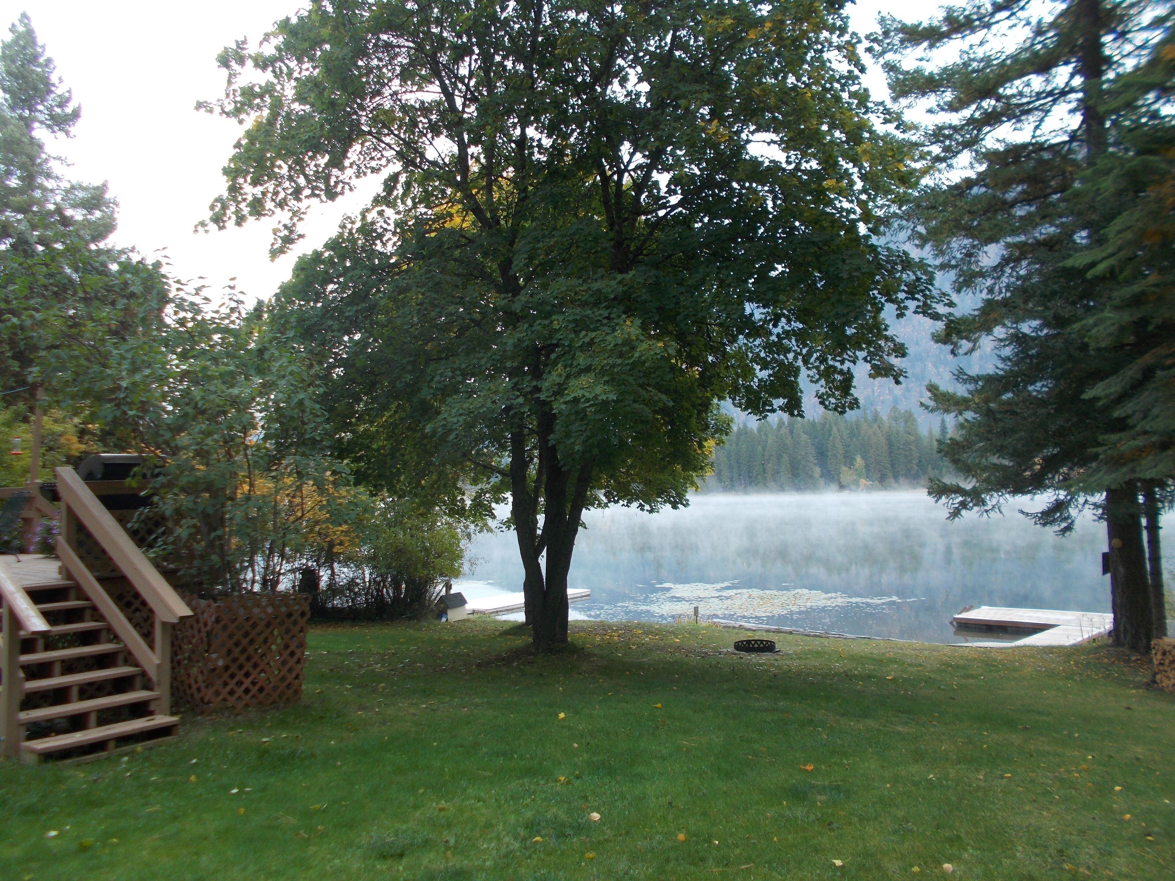 Une propriété située au bord du lac, dotée d’une terrasse en bois, d’un arbre et offrant une vue sur le lac.