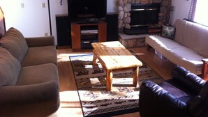 Una sala de estar con chimenea de piedra, una mesa de centro de madera, un sofá y un televisor.