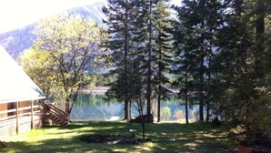 Una cabaña con terraza y vista a un lago rodeado de árboles.