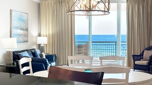 Une chambre d’hôtel moderne avec un balcon donnant sur l’océan, un coin repas et un espace de vie comprenant un canapé et des fauteuils.