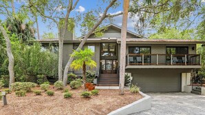 A two-story house with a front porch, a garage, and a well-maintained garden with various plants and a palm tree.