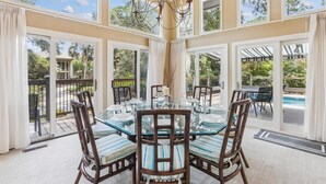 A dining area with a glass table and chairs, large windows, and a view of a swimming pool.