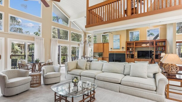 A spacious living room with a large sofa, a glass coffee table, and a balcony with a view of the outdoors.