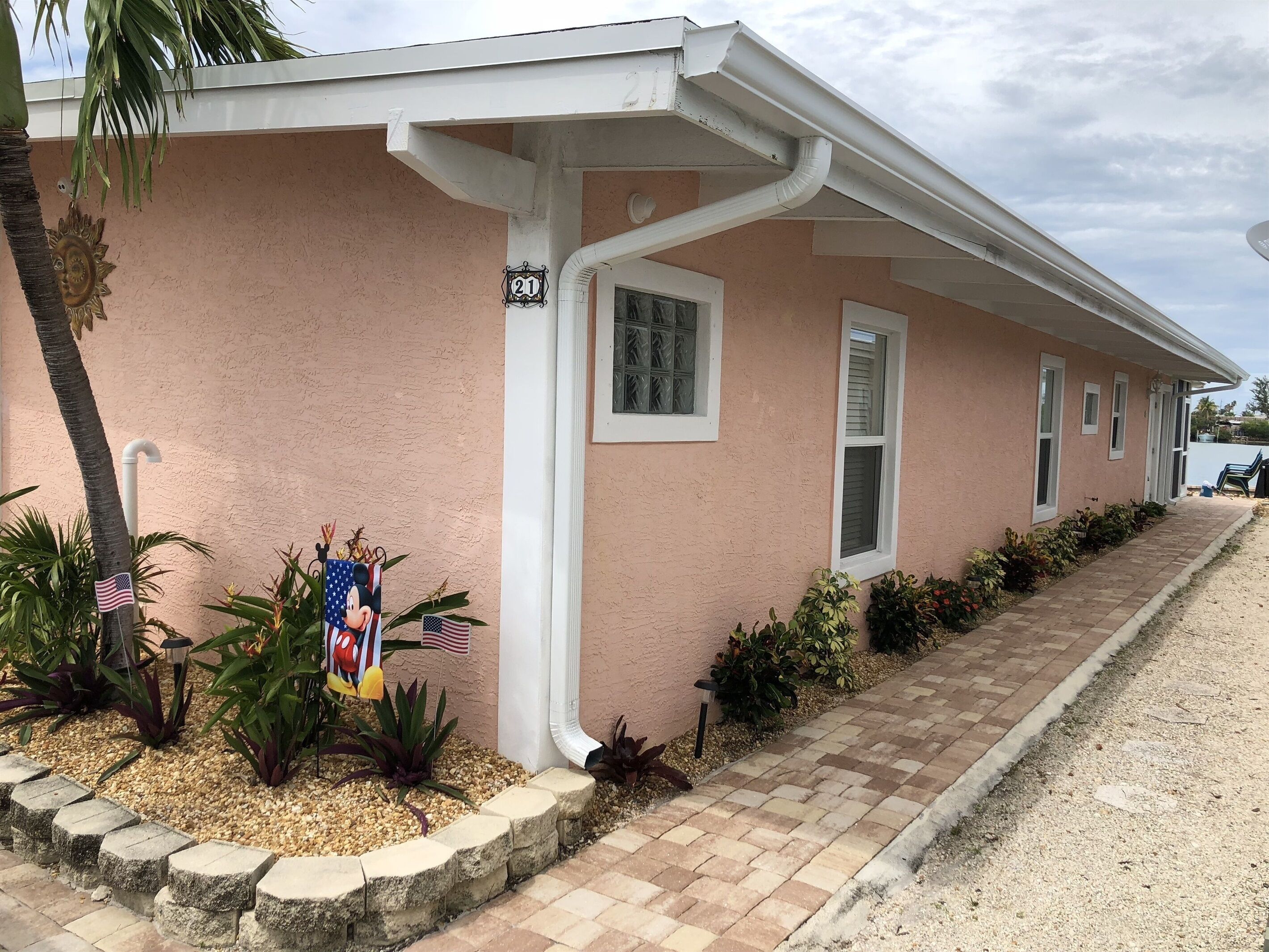 A single-story building with a pink exterior, numbered 21, featuring a small porch with a brick pathway leading to the entrance.