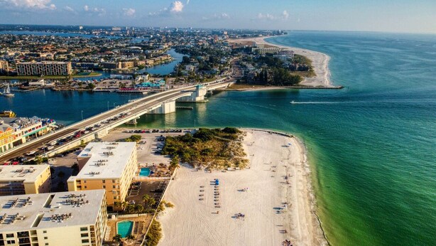 An aerial view of a coastal city with a prominent bridge, a beach, and a marina.