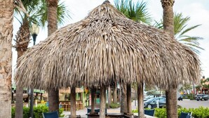 A thatched-roof outdoor bar area with metal chairs and a wooden counter.