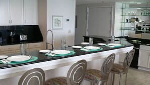 A modern kitchen with a central island, bar stools, and a glass display cabinet. - Spacious Belle Mer 3BR -- 2 Gulf Front Masters -- All with Private Baths (Navarre Beach)