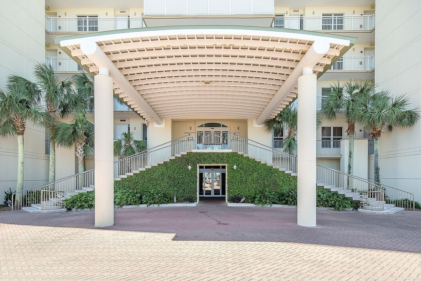 A hotel entrance with a covered staircase, palm trees, and a modern building facade.