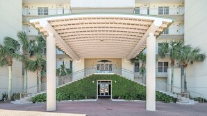 A hotel entrance with a covered staircase, palm trees, and a modern building facade. - Spacious Belle Mer 3BR -- 2 Gulf Front Masters -- All with Private Baths (Navarre Beach)
