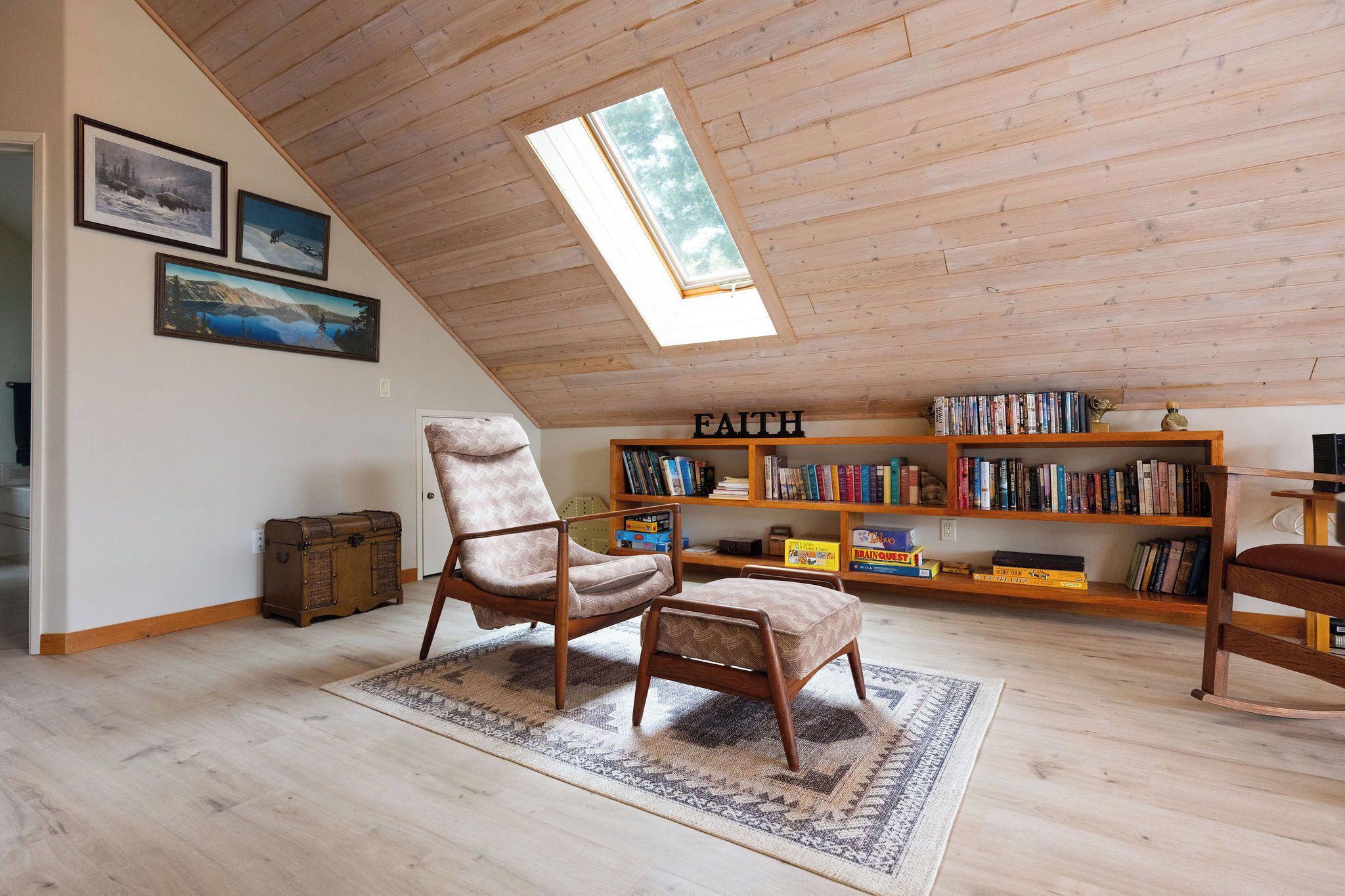 A loft-style room with a sloped ceiling, a skylight, a wooden bookshelf, and a vintage armchair.