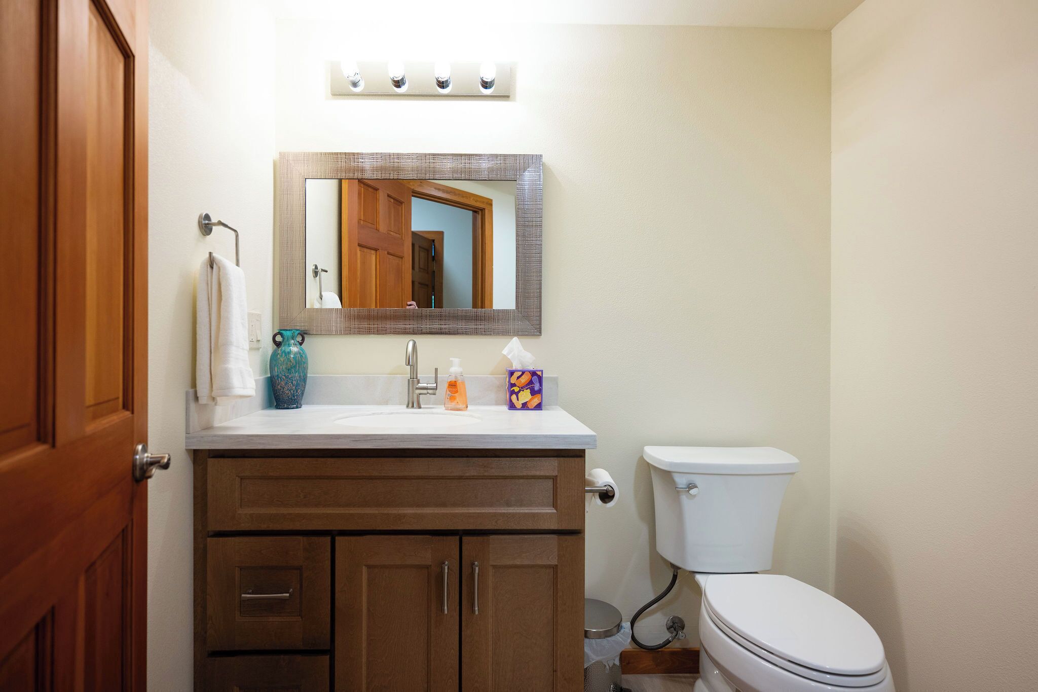 Een badkamer met toilet, wastafel, spiegel en houten kasten.