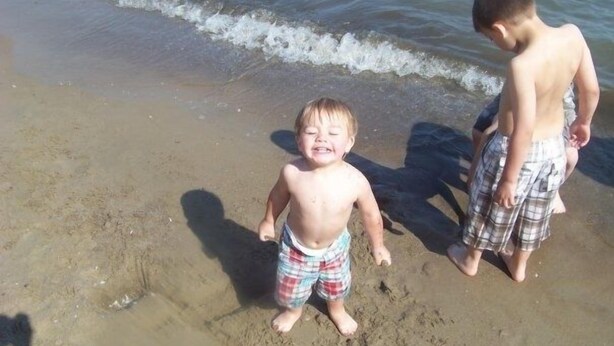 Zwei Kinder spielen am sandigen Strand, im Hintergrund sind Wellen zu sehen.