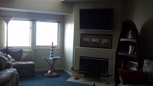Ein Wohnzimmer mit Kamin, einem an der Wand befestigten Fernseher, einem kleinen Tisch mit Dekoration und einem Bücherregal.