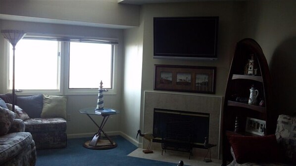 A living room with a fireplace, a television mounted on the wall, a small table with a decorative item, and a bookshelf.